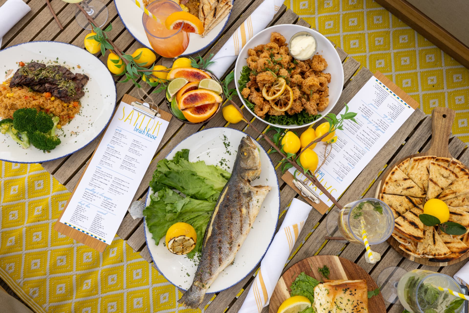 Table spread of grilled fish, calamari, steak, and cocktails at Saylor Beach House