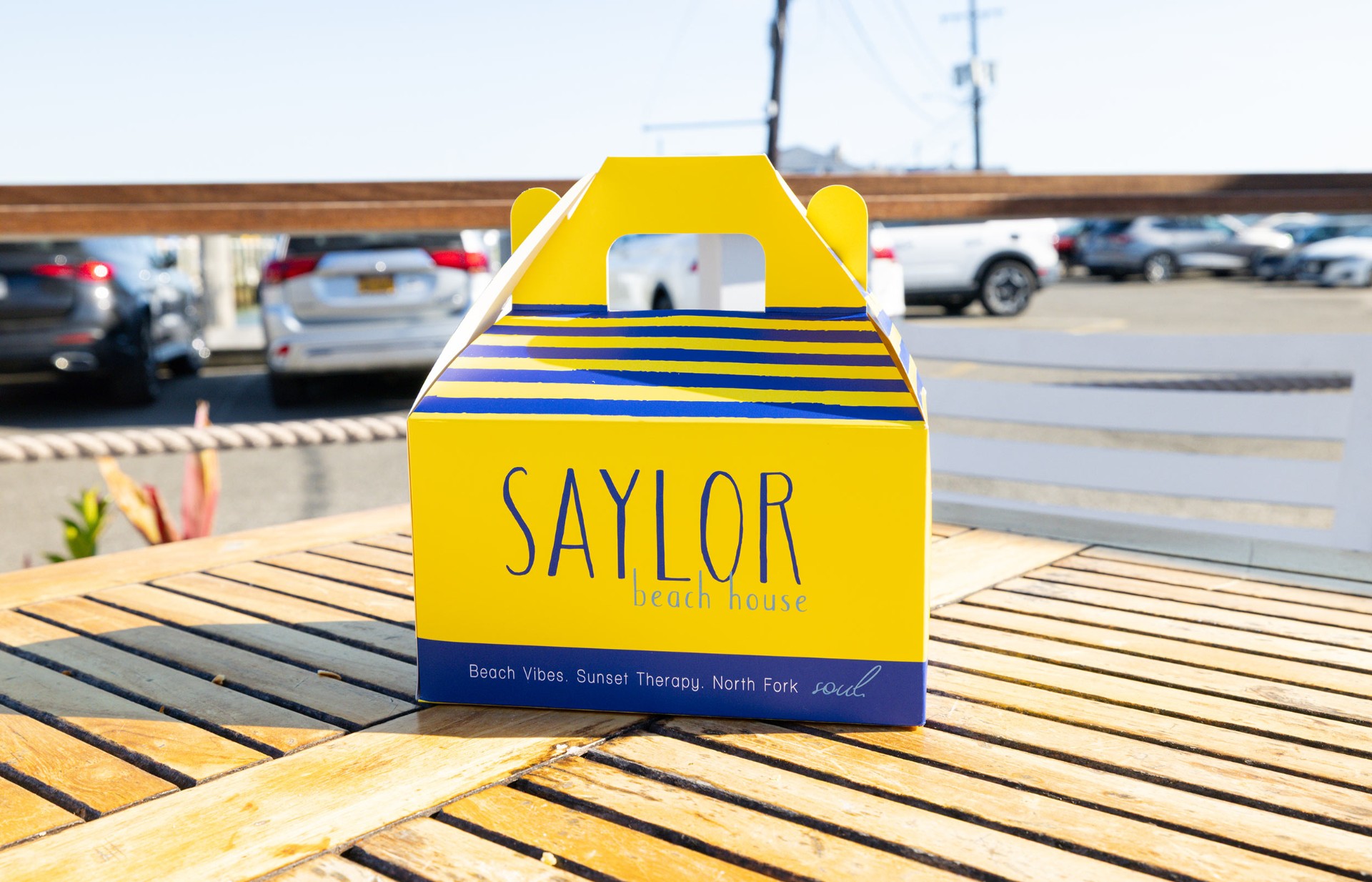 Saylor Beach House signature takeaway box on a dockside table